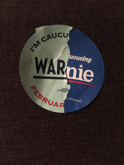 A sticker composed of half of an Elizabeth Warren sticker and half of a Bernie Sanders sticker.  It appears to say something like 'I'm caucusing WARnie'.