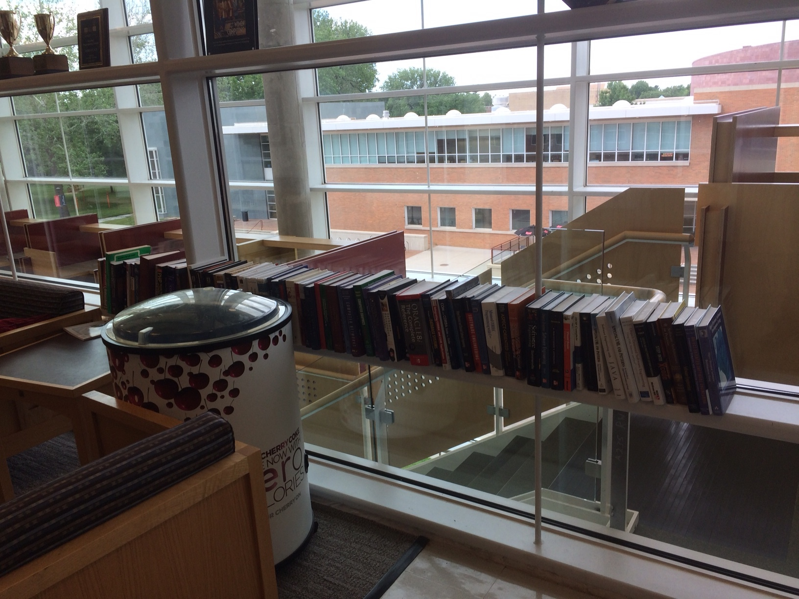 A room with a large glass window with metal shelves in front of the window.  On the shelves are about eight books.