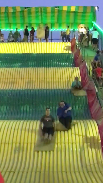 A three-or-so-story slide in yellow and green.  Three people are sliding down.