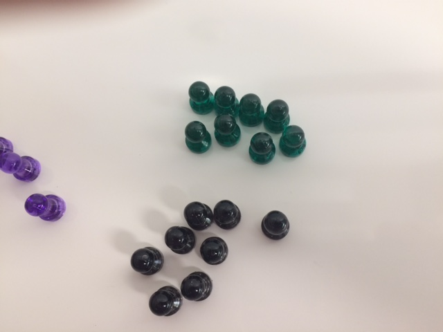 An image with eight dark green plastic magnets, eight black magnets, and a few purple magnets