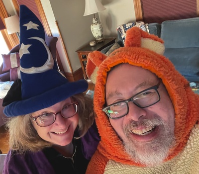 A halloween selfie of Michelle and Sam in their living room. Michelle is in a Mickey Mouse wizard's cap and a purple robe. Sam is in a tigger costume.