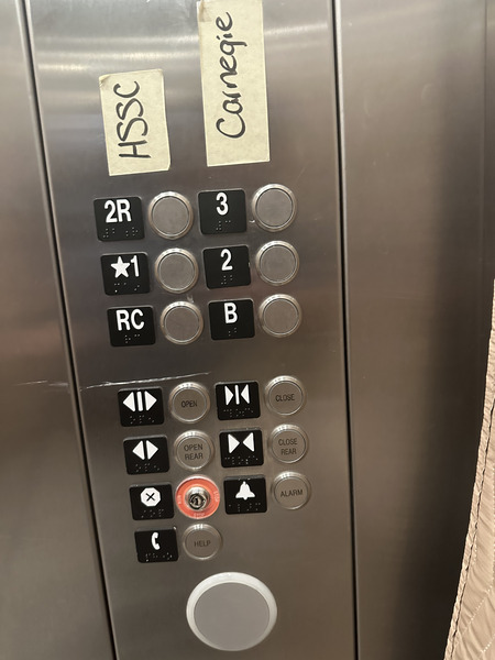 A set of elevator buttons arranged in two columns. The left column has a piece of tape labeling them that reads 'HSSC'. The right column has a piece of tape that says 'Carnegie'. The left column has the buttons '2R', '*1', and 'RC'. The right column has the buttons '3', '2', and 'B'.