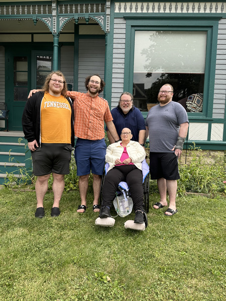 A bald woman in a wheelchair sitting in front of four large men who look happy.