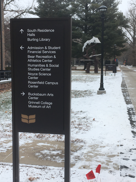 A sign with three arrows: One pointing ahead, one pointing to the left, and one pointing to the right.  The arrow pointing straight ahead is accompanied by two names: 'South Residence Halls' and 'Burling Library'.  The one pointing to the left is accompanied by five names: 'Admission & Student Financial Services', 'Bear Recreation & Athletics Center', 'Humanities and Social Studies Center', 'Noyce Science Center', and 'Rosenfield Campus Center'.  The arrow pointing to the right is accompanied by two names: 'Bucksbaum Arts Center' and 'Grinnell College Museum of Art'