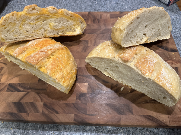 Two round loaves of white bread, each cut in half and arranged. The one on the left shows swirls of yellow cheese.