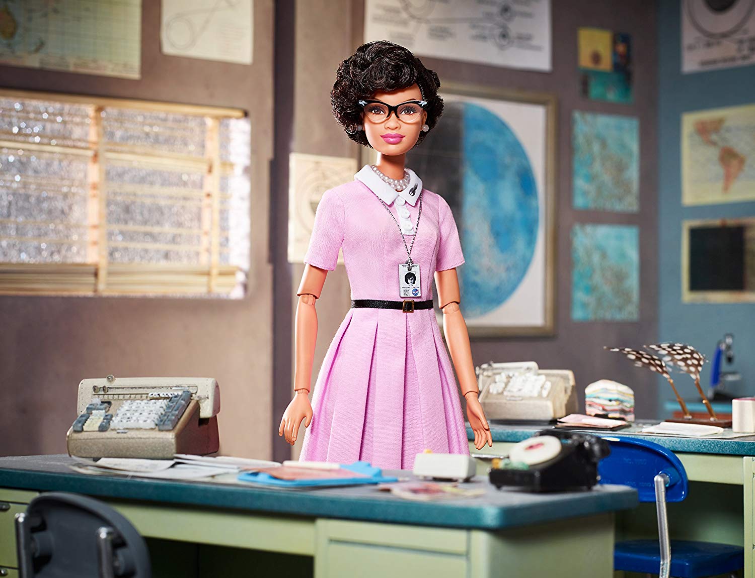 A Barbie doll that looks vaguely like Katherine Johnson, or at least the actress who portrayed Katherine Johnson in the movie 'Hidden Figures'.  She is placed in an office setting that includes adding machines on each desk and an old dial telephone.
