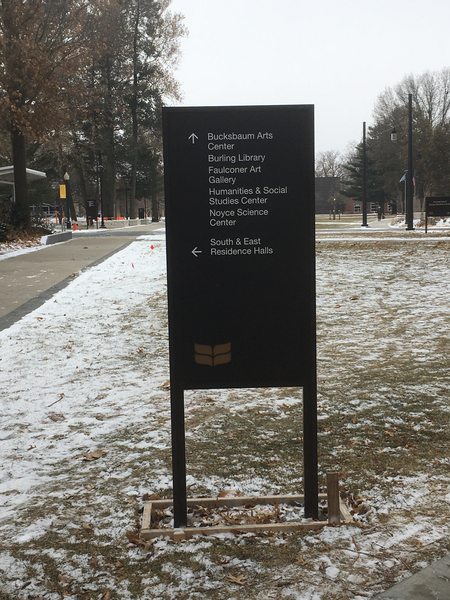 A photo with a sign that has an arrow pointing forward and five things listed: 'Bucksbaum Arts Center', 'Burling Library', 'Faulconer Art Gallery', 'Humanities and Social Studies Center', and 'Noyce Science Center'.  There is also an arrow pointing to the left that reads 'South & East Residence Halls'